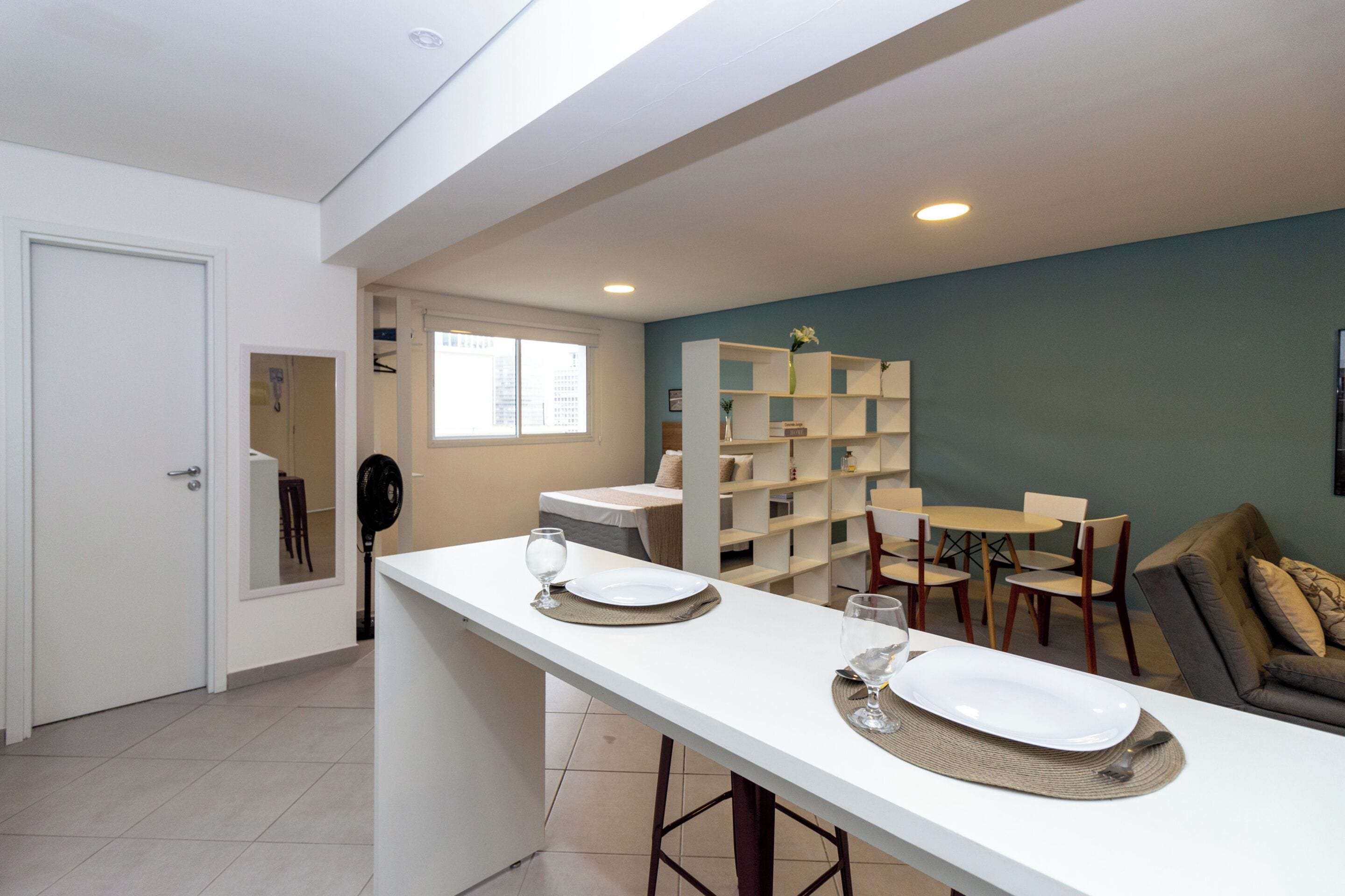 A modern kitchen with a white countertop, a dining area with a table and chairs, and a sofa in the living area.