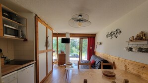 A cozy room with a wooden dining table, chairs, a TV, and a sliding glass door leading to an outdoor area. - Cosy apt 4 ppl, near the ski runs (Chamrousse)