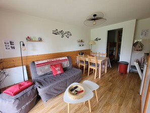 A cozy living room with a sofa, a dining table, and a small TV stand.