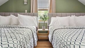 Quarto com duas camas, uma mesinha e uma janela com cortinas.