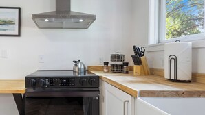 Uma cozinha moderna com exaustor de aço inoxidável, forno embutido e janela com vista para árvores.