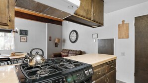 Una cucina con piano cottura a gas, pensili e basi in legno, una sveglia e un frigorifero.