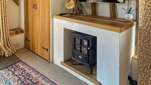 Une pièce avec une armoire en bois, un téléviseur encastré, un petit poêle noir et un tapis à motifs.