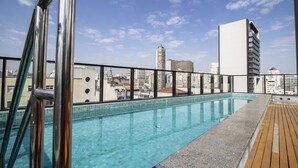 A rooftop pool with a city view, metal railings, and a wooden deck. - Aurora Paulistana  (São Paulo)