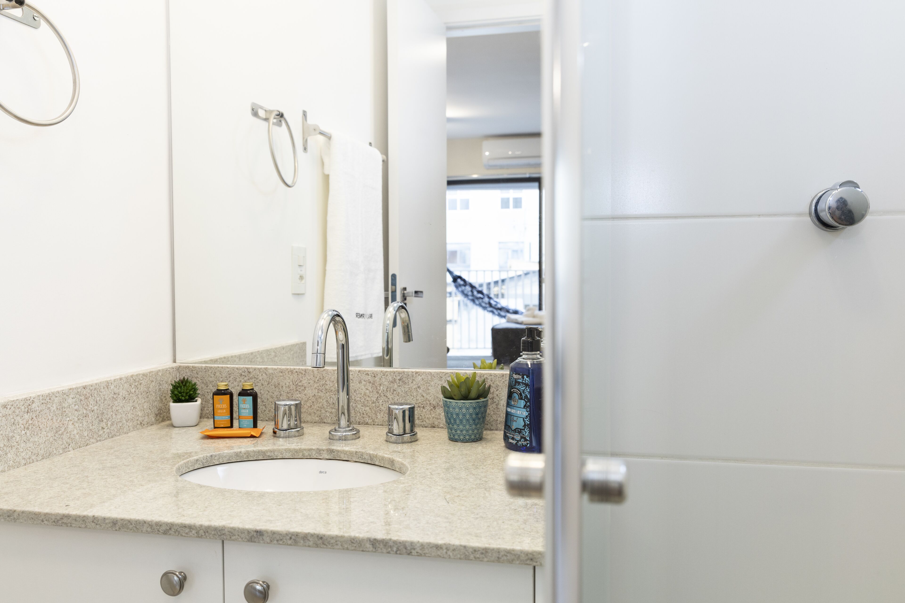 Un baño moderno con encimera de granito, lavabo blanco, espejo y zona de ducha visible a través de una puerta abierta.