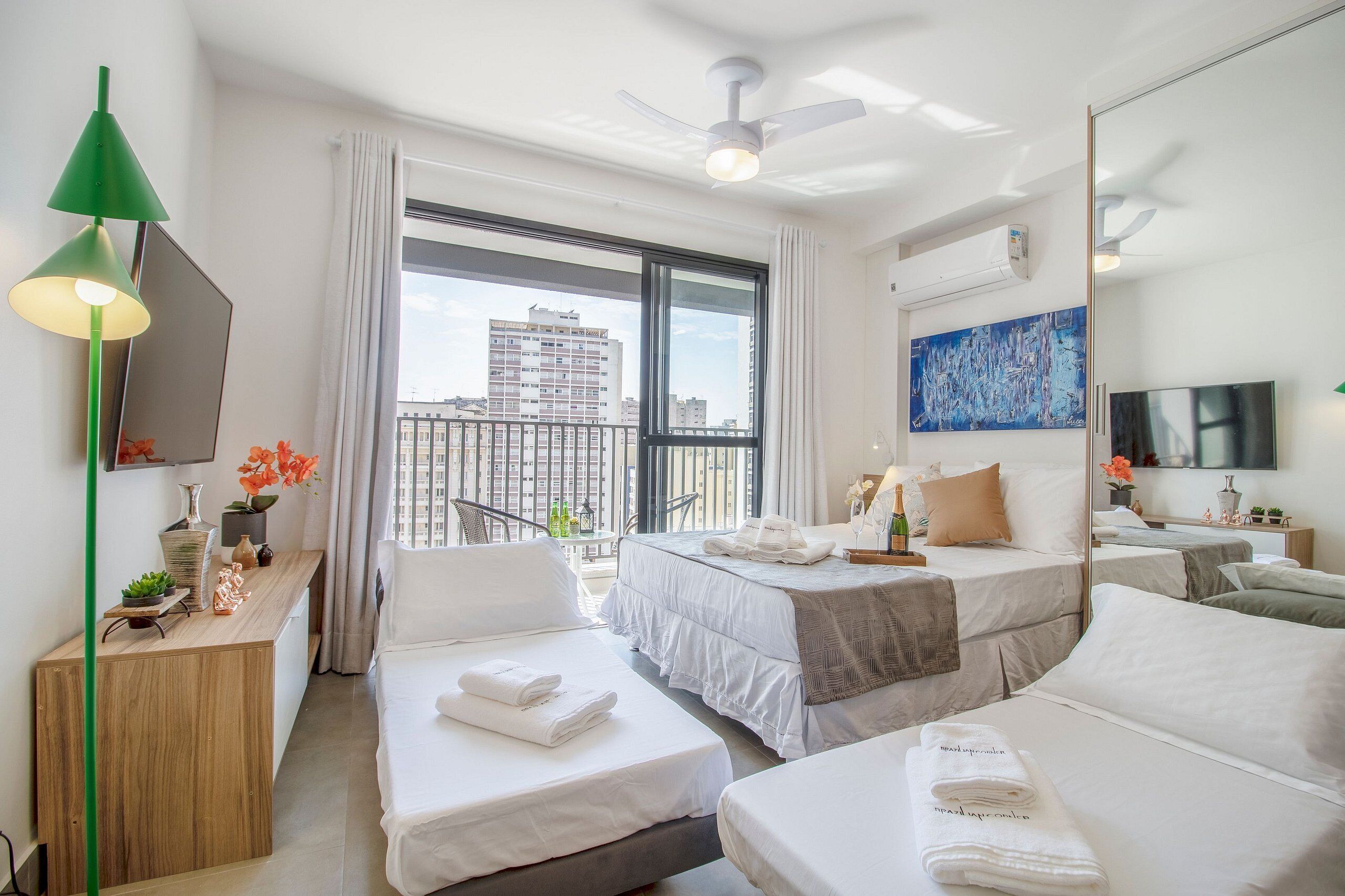 A hotel room with two beds, a desk, a chair, a large window with a city view, a ceiling fan, and a flat-screen TV.