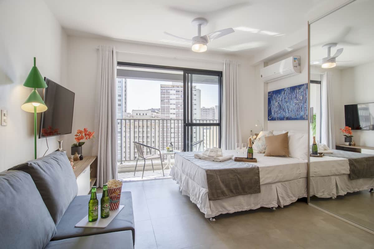 Ein modernes Hotelzimmer mit Balkon, einem Bett, einer Couch, einem Fernseher und einem Essbereich.
