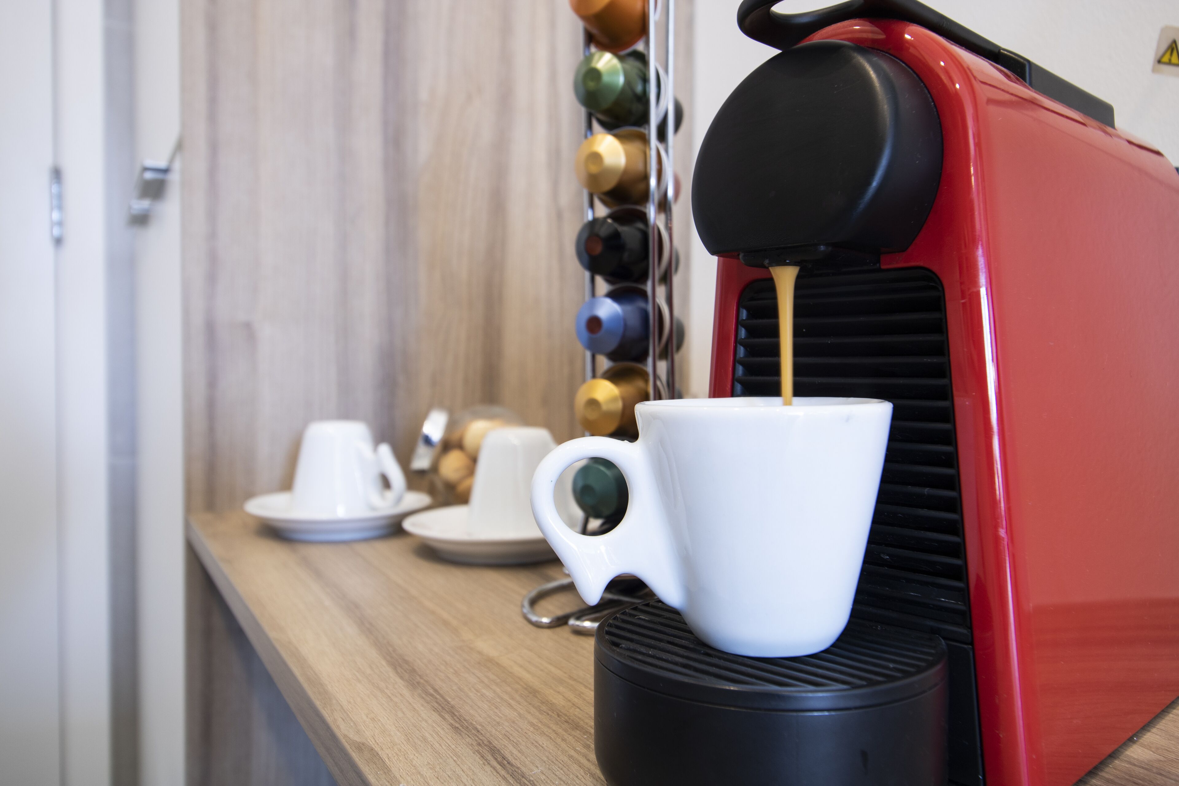 Une machine à café verse du café dans une tasse blanche posée sur un comptoir en bois.