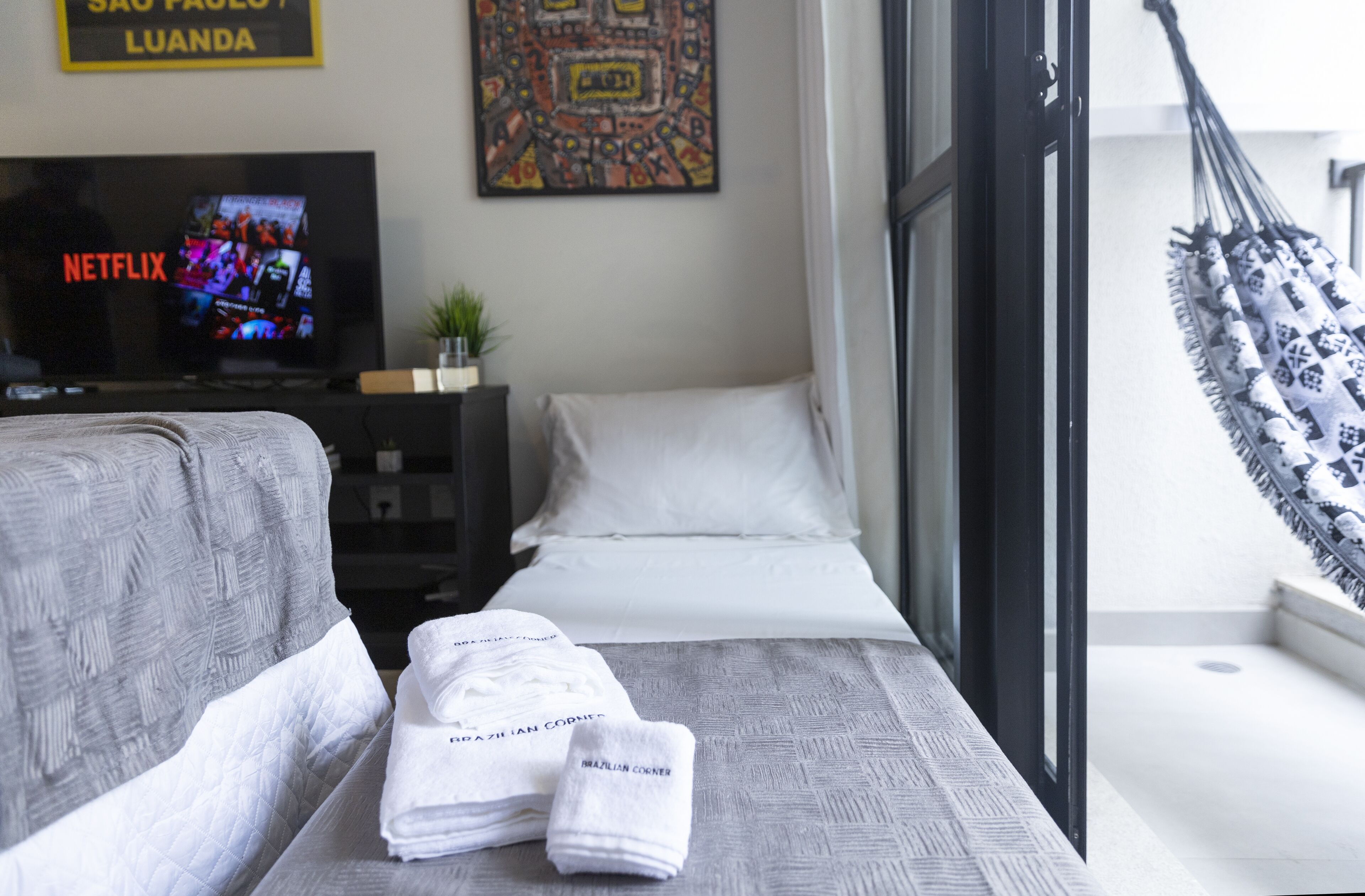 Ein Hotelzimmer mit einem Bett, einem Fernseher, der Netflix anzeigt, einem Wandbild und einer Hängematte.