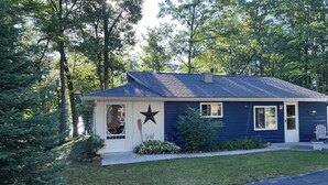 A single-story house with a dark blue exterior, a white front door, and a star decoration on the door. - The Bluebird Cottage.  Just go down 400 feet and jump in lake . (Roscommon)