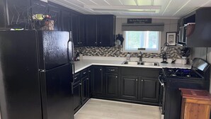 A kitchen with black cabinets, a white countertop, a black refrigerator, a stove, and a window with a view of the outside. - The Bluebird Cottage.  Just go down 400 feet and jump in lake . (Roscommon)