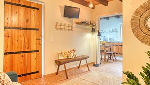 A wooden door, a bench, a television mounted on the wall, and a kitchen area with a table and chairs.
