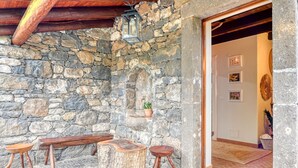 A stone wall with a wooden bench and stools, a lantern, and a door leading inside.