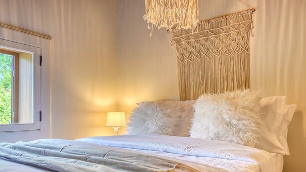 A neatly made bed with fluffy pillows and a macramé wall hanging.