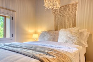 Een net opgemaakt bed met zachte kussens en een macramé wanddecoratie.