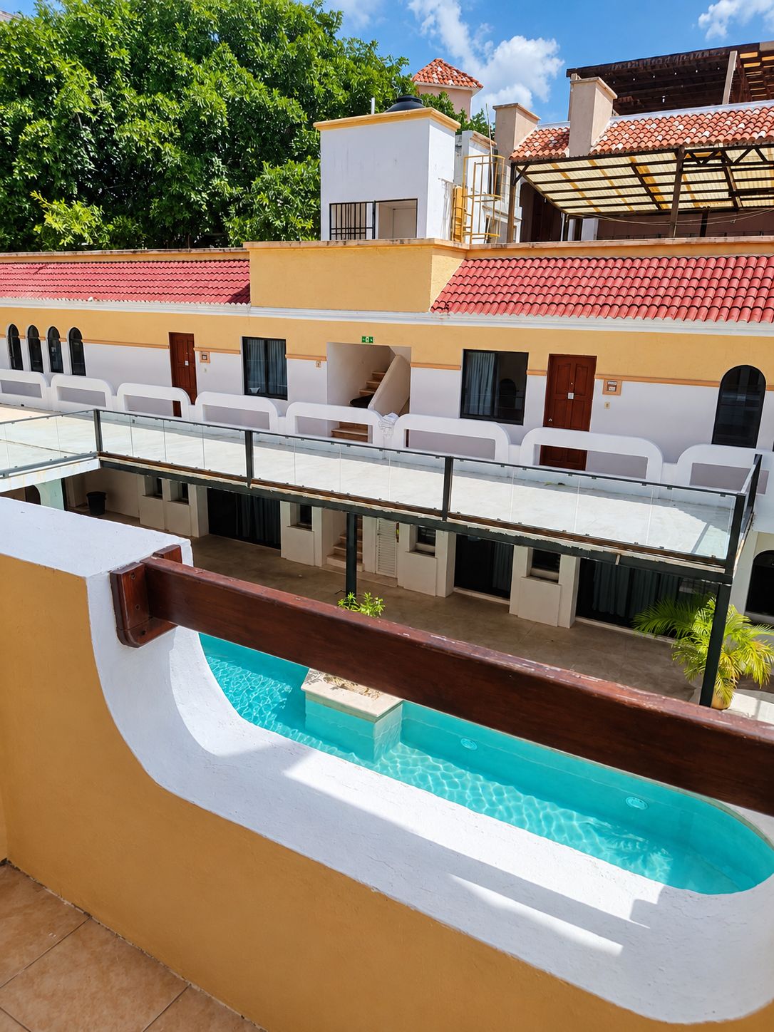 A hotel with a swimming pool, outdoor seating, and a red-tiled roof.
