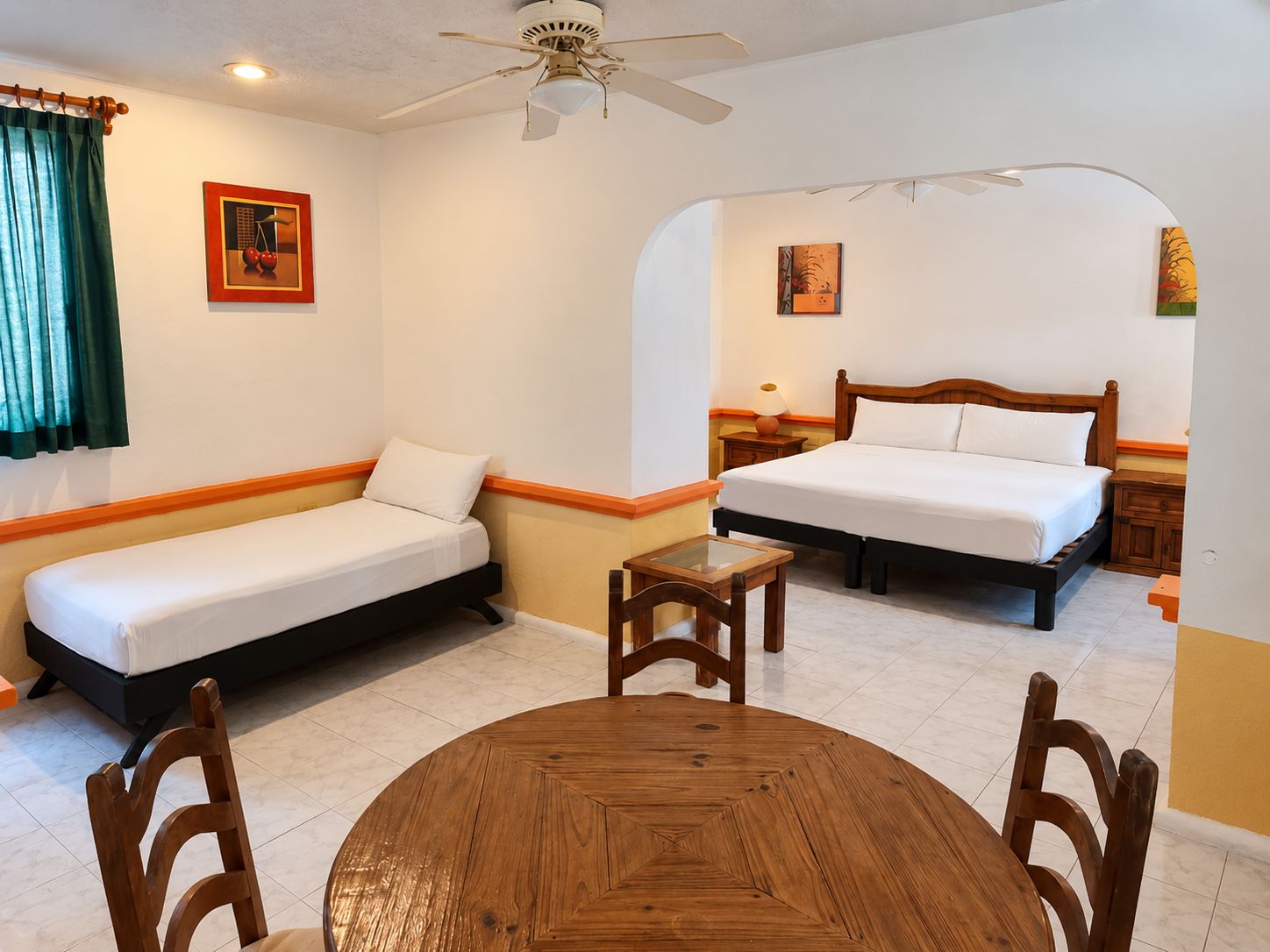 Quarto de hotel com duas camas, uma mesinha e um ventilador de teto.