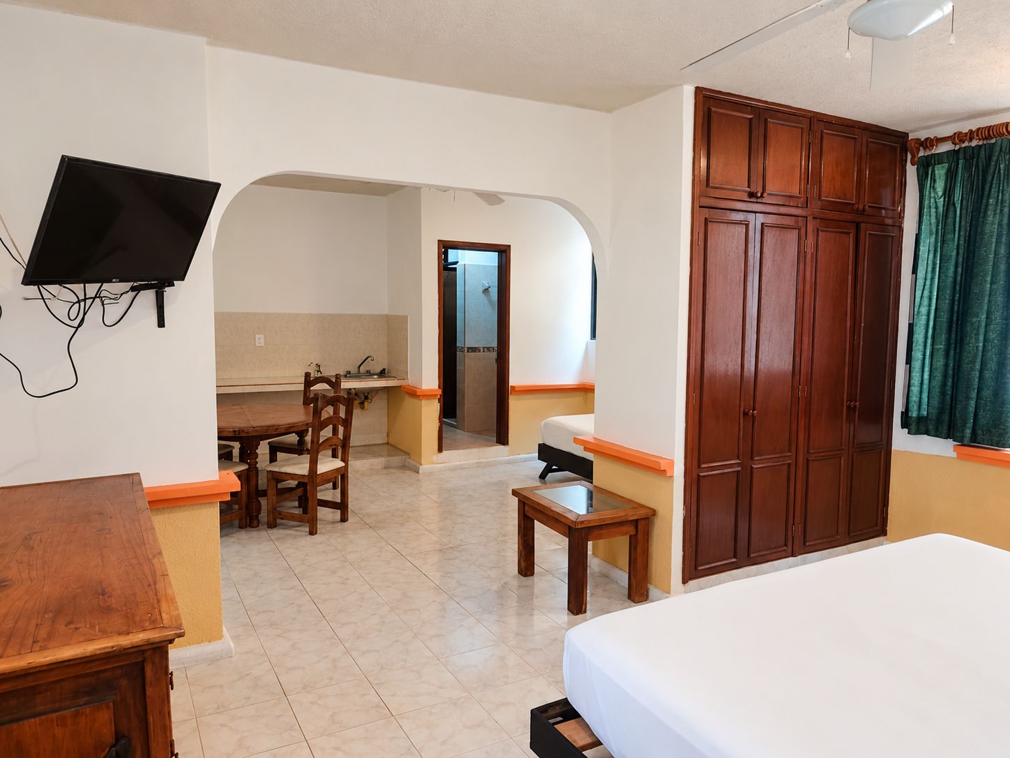 Quarto de hotel com cama, escrivaninha, cadeira, televisão presa à parede e armário.