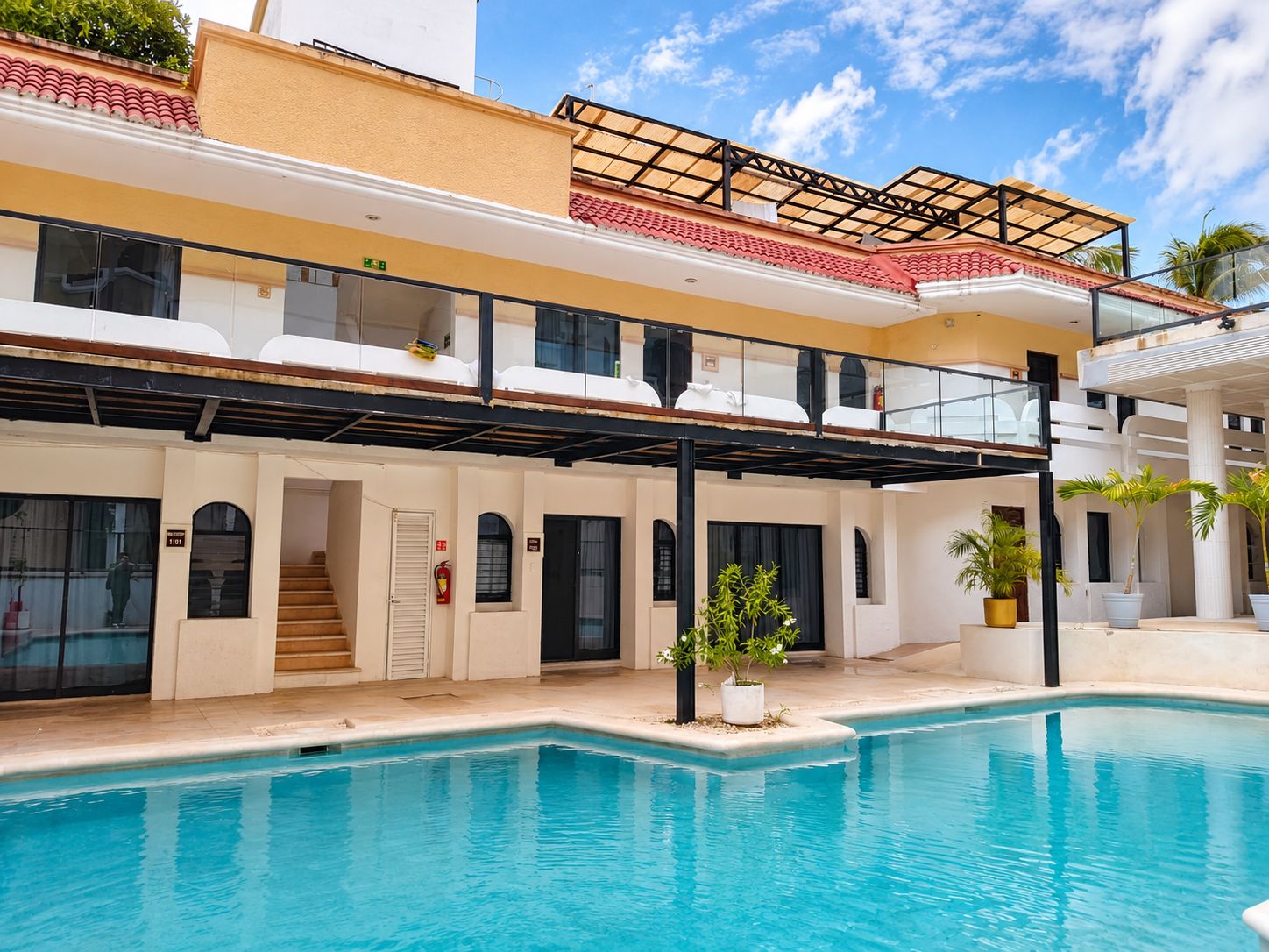 Un edificio de dos pisos con piscina, balcones y una zona exterior cubierta.