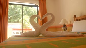 Een hotelkamer met een bed, een handdoekarrangement in de vorm van een hart, een lamp en uitzicht op groen buiten.