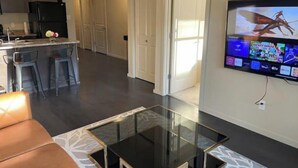 A modern living room with a glass coffee table, a sofa, and a TV displaying a cartoon.
