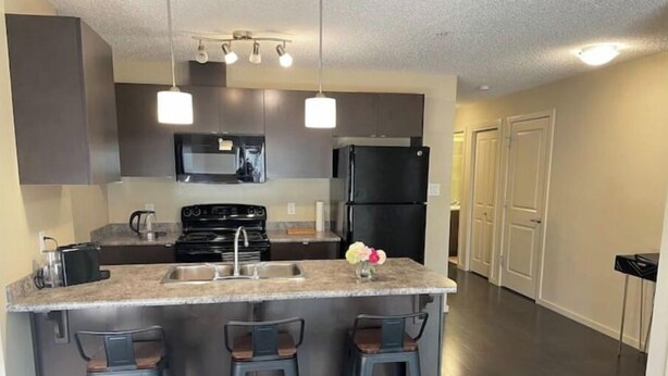 A modern kitchen with a central island, bar stools, stainless steel appliances, and pendant lighting.