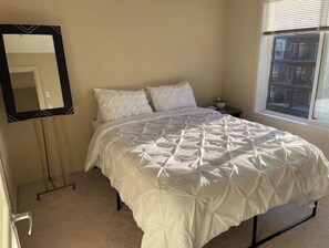 A bedroom with a bed, a nightstand, a mirror, and a window. - Chic & Modern Windermere Condo (Edmonton)