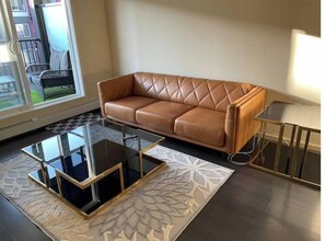 Una sala de estar moderna con un sofá de cuero marrón, una mesa de centro de vidrio y una alfombra estampada.