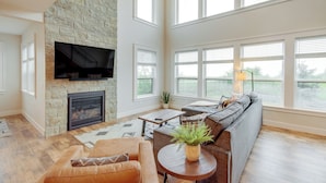 A spacious living room with a stone fireplace, a large flat-screen TV, a comfortable sofa, and a view through large windows. - Hot Tub & Deck at Red Lodge Retreat (Red Lodge)