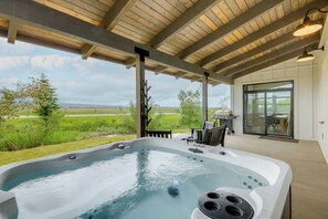 Een hottub onder een houten pergola met uitzicht op een grasveld en heuvels in de verte.