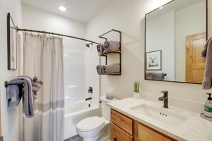A modern bathroom with a bathtub, toilet, and vanity with a sink and mirror. - Hot Tub & Deck at Red Lodge Retreat (Red Lodge)