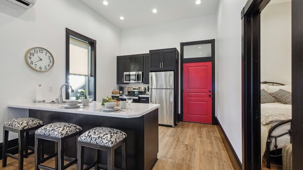 Una cocina moderna con una isla central, armarios oscuros, una puerta roja y un reloj en la pared.