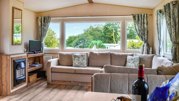 A cozy living room with a large window, a ceiling fan, and a television on a wooden stand. - 2 bedroom accommodation in Kippford, near Sandyhills (Kippford, near Sandyhills)