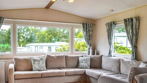 A cozy living room with a sectional sofa, large windows, and a view of greenery outside. - 2 bedroom accommodation in Kippford, near Sandyhills (Kippford, near Sandyhills)