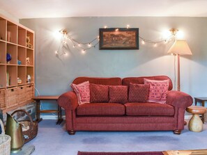 Una sala de estar acogedora con un sofá rojo, una estantería de madera, un cuadro enmarcado y luces de cadena.