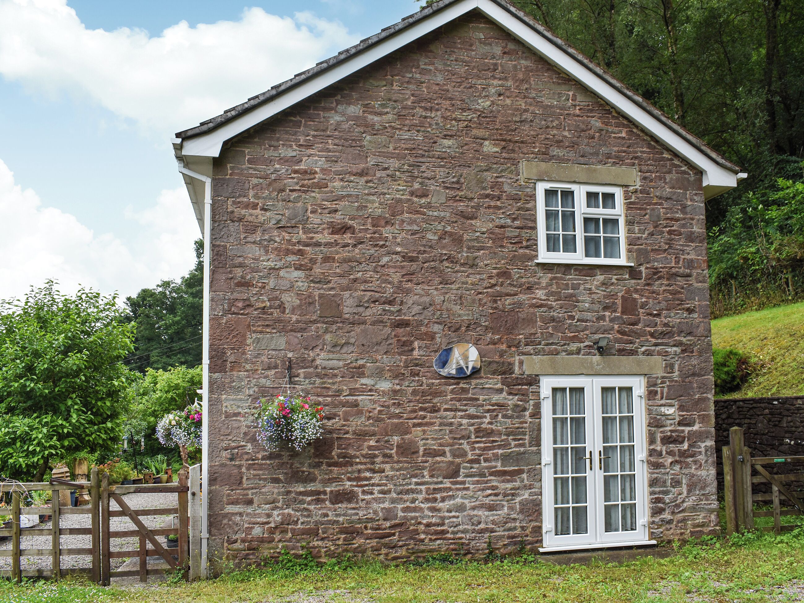 A stone building with a white door and window, surrounded by greenery.