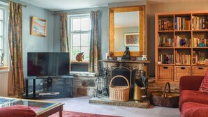 Ein Wohnzimmer mit Kamin, Bücherregalen, einem Fernseher und einem roten Teppich.