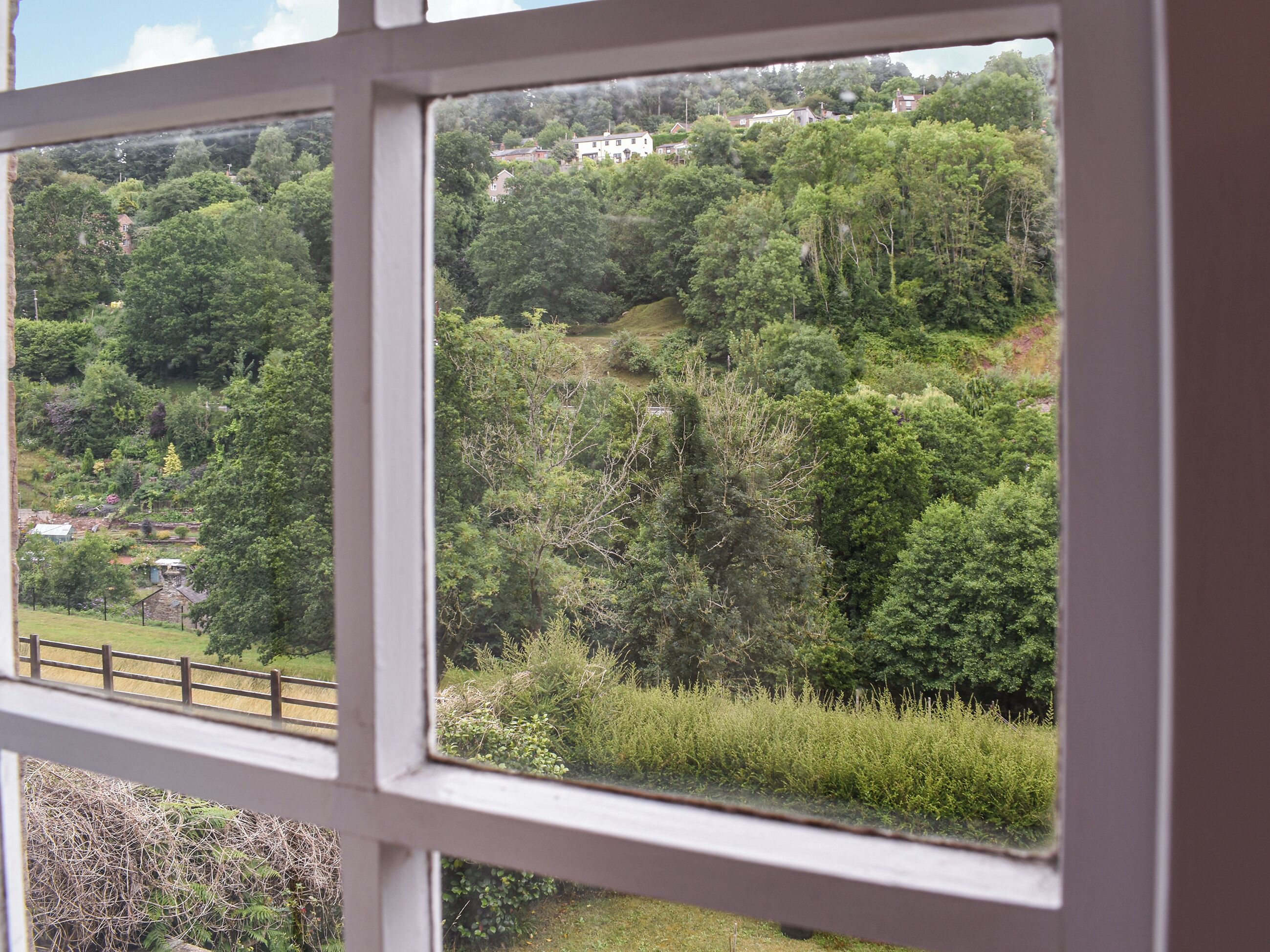 A window view of a lush green landscape with a white building in the distance.