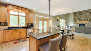 A spacious kitchen with wooden cabinets, a central island, and a dining area with chairs. - Riverfront Bliss in Rice Lake: Deck, Grill & Hike! (Rice Lake)