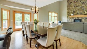 A dining area with a large table and chairs, a chandelier, and a stone wall. - Riverfront Bliss in Rice Lake: Deck, Grill & Hike! (Rice Lake)