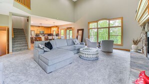 A spacious living room with a grey sectional sofa, a patterned ottoman, and a large window providing natural light. - Riverfront Bliss in Rice Lake: Deck, Grill & Hike! (Rice Lake)