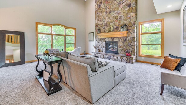 A living room with a stone fireplace, a sofa, a dining table, and large windows. - Riverfront Bliss in Rice Lake: Deck, Grill & Hike! (Rice Lake)