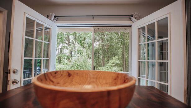 A wooden bowl on a dark countertop with a view of a forest through open doors. - Mins To AVL, Secluded, Firepit, Family Friendly (Asheville)