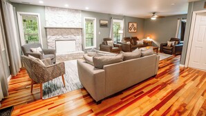 A spacious living room with a stone fireplace, hardwood flooring, and a mix of seating options including a sofa and armchairs. - Mins To AVL, Secluded, Firepit, Family Friendly (Asheville)