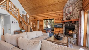 A log cabin interior with a stone fireplace, a wooden staircase, and a beige sectional sofa. - 3 Cubs Lakefront Cabin  (Big Bear Lake)