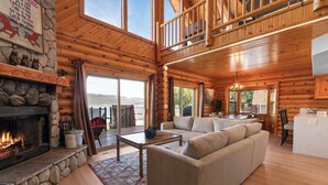 A log cabin interior with a stone fireplace, a sofa, a dining table, and a kitchen area. - 3 Cubs Lakefront Cabin  (Big Bear Lake)