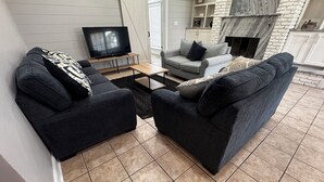 Een woonkamer met twee donkere banken, een salontafel, een tv op een meubel en een open haard.