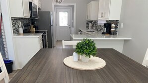 Een moderne keuken met witte kasten, een donker houten eettafel en een potplant.