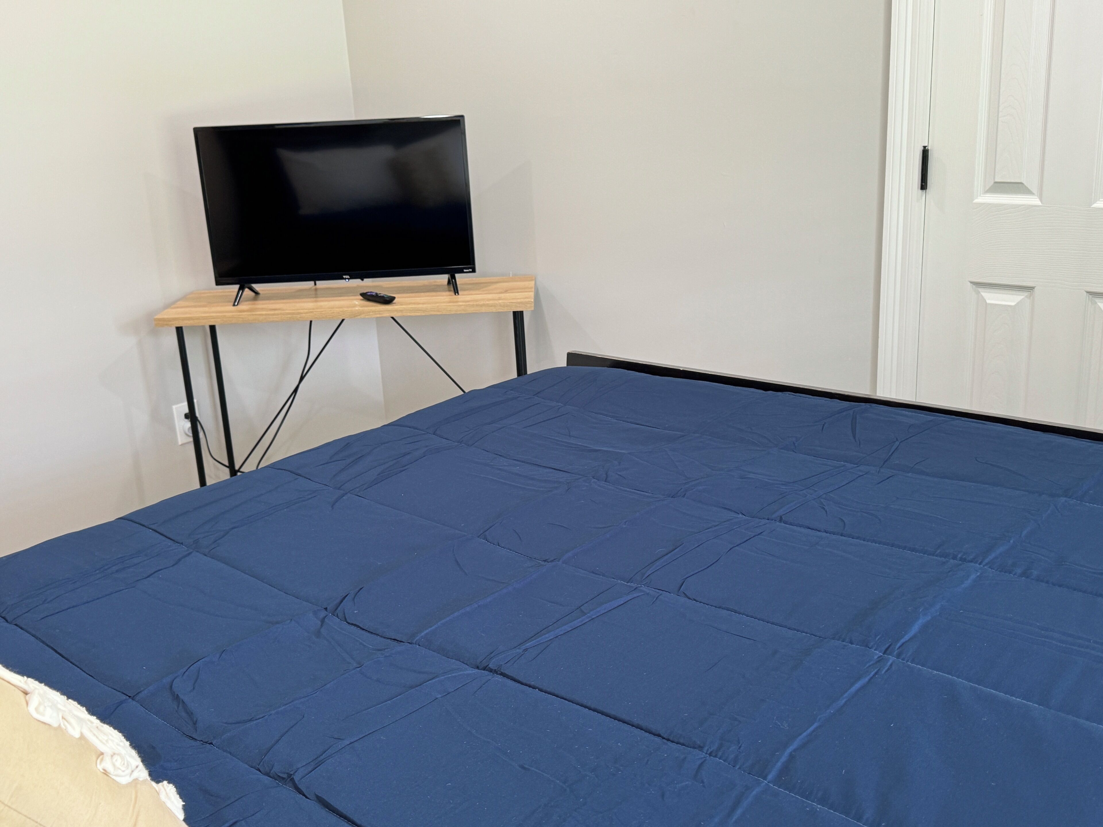 Un dormitorio con una cama, un televisor sobre un mueble y una puerta blanca.