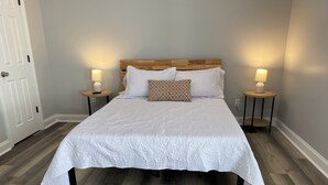 Een netjes opgemaakt bed met een witte quilt, twee nachtkastjes met lampen en een houten hoofdbord.